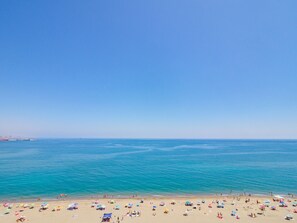 A beach with a clear blue sky, calm sea, and numerous colorful umbrellas.