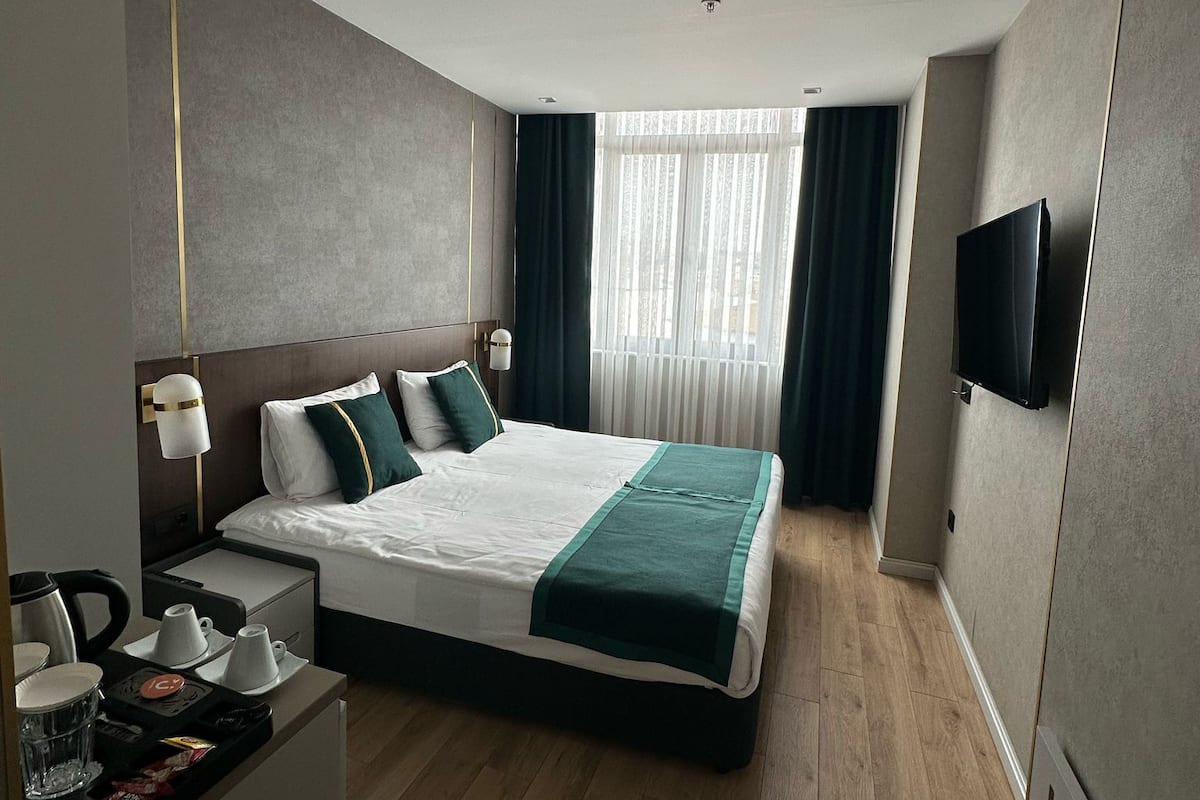 Ein modernes Hotelzimmer mit einem großen Bett, Nachttischen, einem Flachbildfernseher und einem Fenster mit Vorhängen.