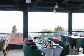 Un comedor con una mesa lista para dos, sillas y vista al mar.