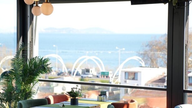 A restaurant with a view of the sea, featuring round tables, chairs, and hanging lights. - Costera Hotel (Istanbul)
