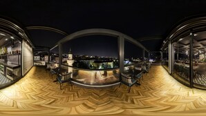 A modern rooftop bar with a panoramic city view, featuring a wooden herringbone floor and glass-enclosed seating areas. - Costera Hotel (Istanbul)