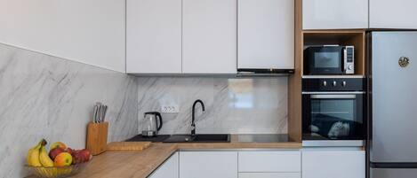 Una cocina moderna con armarios blancos, una encimera de madera, un lavabo, un hervidor, un microondas y un refrigerador.