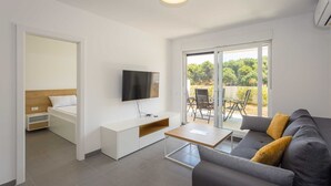Un salon moderne avec un canapé gris, un téléviseur à écran plat, une table basse en bois et une porte-fenêtre coulissante donnant sur un espace extérieur.