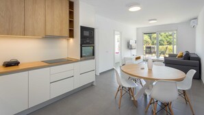 Une cuisine moderne avec des armoires blanches, un plan de travail en bois et un four encastré. On y trouve également un coin repas avec une table ronde en bois et des chaises blanches.