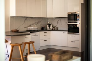 Eine moderne Küche mit weißen Schränken, einer Marmor-Spritzschutzwand, einem eingebauten Ofen und Holzbarhocker.