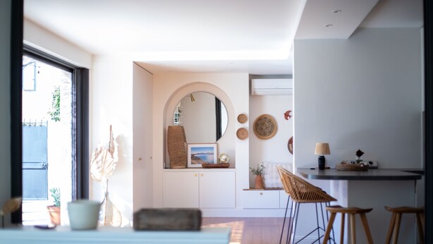 Ein modernes Interieur mit Küchenzeile, einem Essbereich mit Hockern und einem großen Spiegel.
