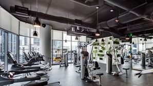 Une salle de sport équipée de tapis de course, d’appareils d’exercice et de grandes fenêtres donnant sur la ville.