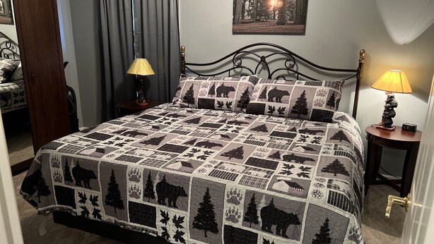 Un dormitorio con una cama, dos mesitas de noche, una lámpara, un cuadro en la pared y una puerta.