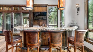 A kitchen with a large island, bar stools, and pendant lighting. - Luxury Sunriver Estate | 5 Kings + Bunk Rm | Huge Spa & Arcade | Chef's Kitchen (Sunriver)