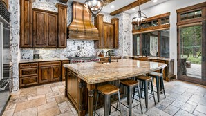 A spacious kitchen with a large island, wooden cabinets, and a stone backsplash. - Luxury Sunriver Estate | 5 Kings + Bunk Rm | Huge Spa & Arcade | Chef's Kitchen (Sunriver)