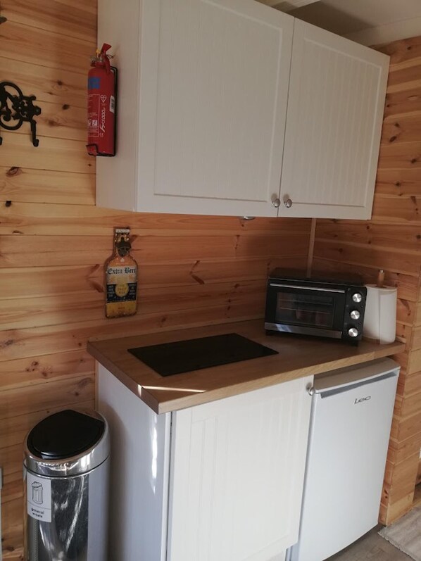 Uma cozinha compacta com micro-ondas, mini-geladeira, lixeira e uma garrafa de cerveja.