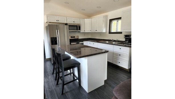 Een moderne keuken met witte kasten, een granieten aanrechtblad en een centraal eiland met barstoelen.