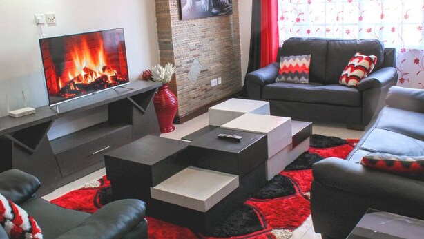 Ein modernes Wohnzimmer mit Flachbildfernseher, Kamin, einem schwarzen Ledersofa und einem Teppich in Rot und Schwarz.