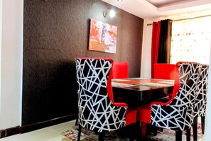 Un comedor con una mesa redonda y sillas de patrones geométricos, una pared oscura y un cuadro sobre la mesa.