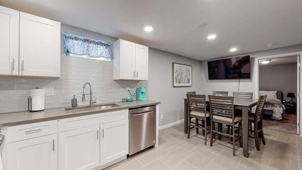 A modern kitchen with white cabinets, a stainless steel dishwasher, and a dining area with wooden chairs and a table. - Great Lower Unit with Spacious Yard and Sunroom (Denver)