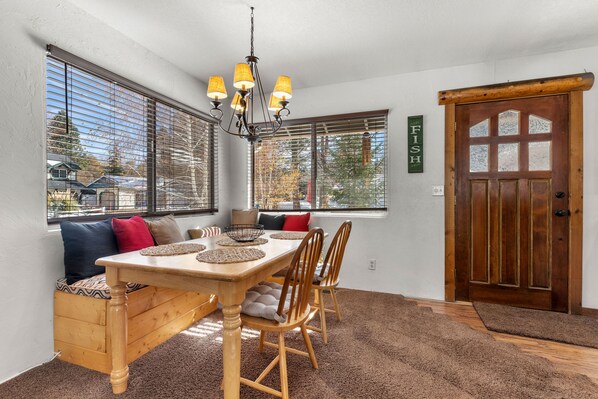 A dining area with a wooden table, four chairs, a chandelier, and a bench with cushions. - Eagle Point Estates, 1/4 MILE TO SKI RESORT! Fenced yard and Garage (Big Bear Lake)
