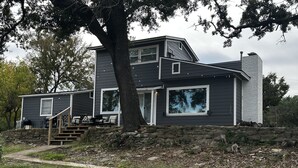 A two-story house with a stone retaining wall, a staircase leading to the entrance, and a large tree in front. - Waterfront Property on PK - 7 miles away from Rocker B baseball facility  (Graford)