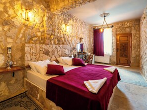 A stone-walled bedroom with a bed, a nightstand, a window with curtains, and a wooden door. - Ala Stone Hotel (Nevsehir)