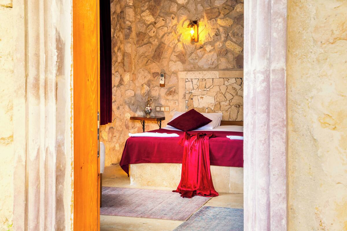 Un dormitorio con paredes de piedra, una cama, una mesita de noche y un vestido rojo en el suelo.