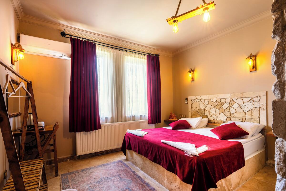 Un dormitorio con cama, un radiador, una silla de madera, un perchero y una pared de piedra.