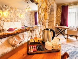 Habitación con paredes de piedra, una mesa de madera, una tetera, tazas y una bandeja con aperitivos.