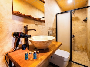 Un baño con un lavabo de piedra grande, un secador de pelo y varias botellas sobre una encimera de madera.