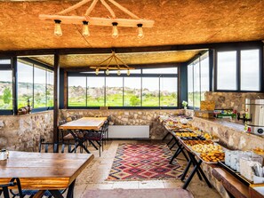 A rustic dining area with a stone wall, a wooden table, and a buffet with various food items. - Ala Stone Hotel (Nevsehir)