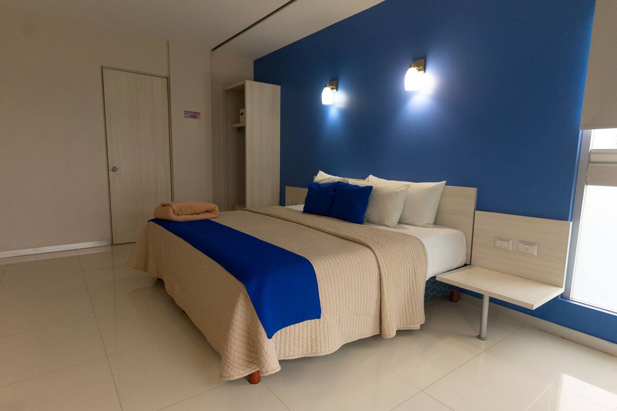 Un dormitorio moderno con una cama grande, un banco y una pared azul destacada.