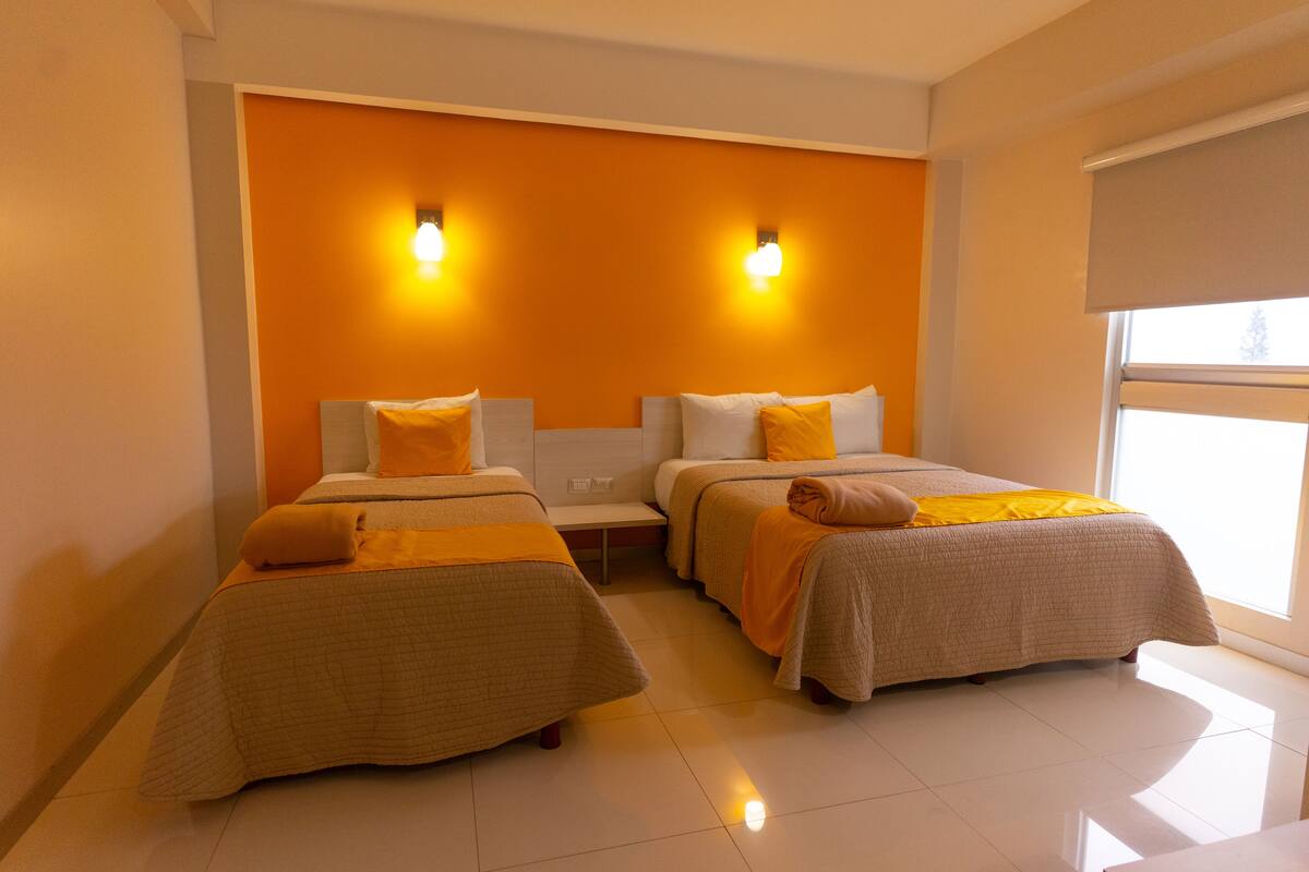 Habitación de hotel con dos camas, cada una con cabecera, mesita de noche y ventana con persiana.