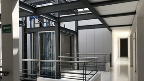 Un interior moderno con un ascensor de vidrio, barandillas de metal y un piso limpio con baldosas.