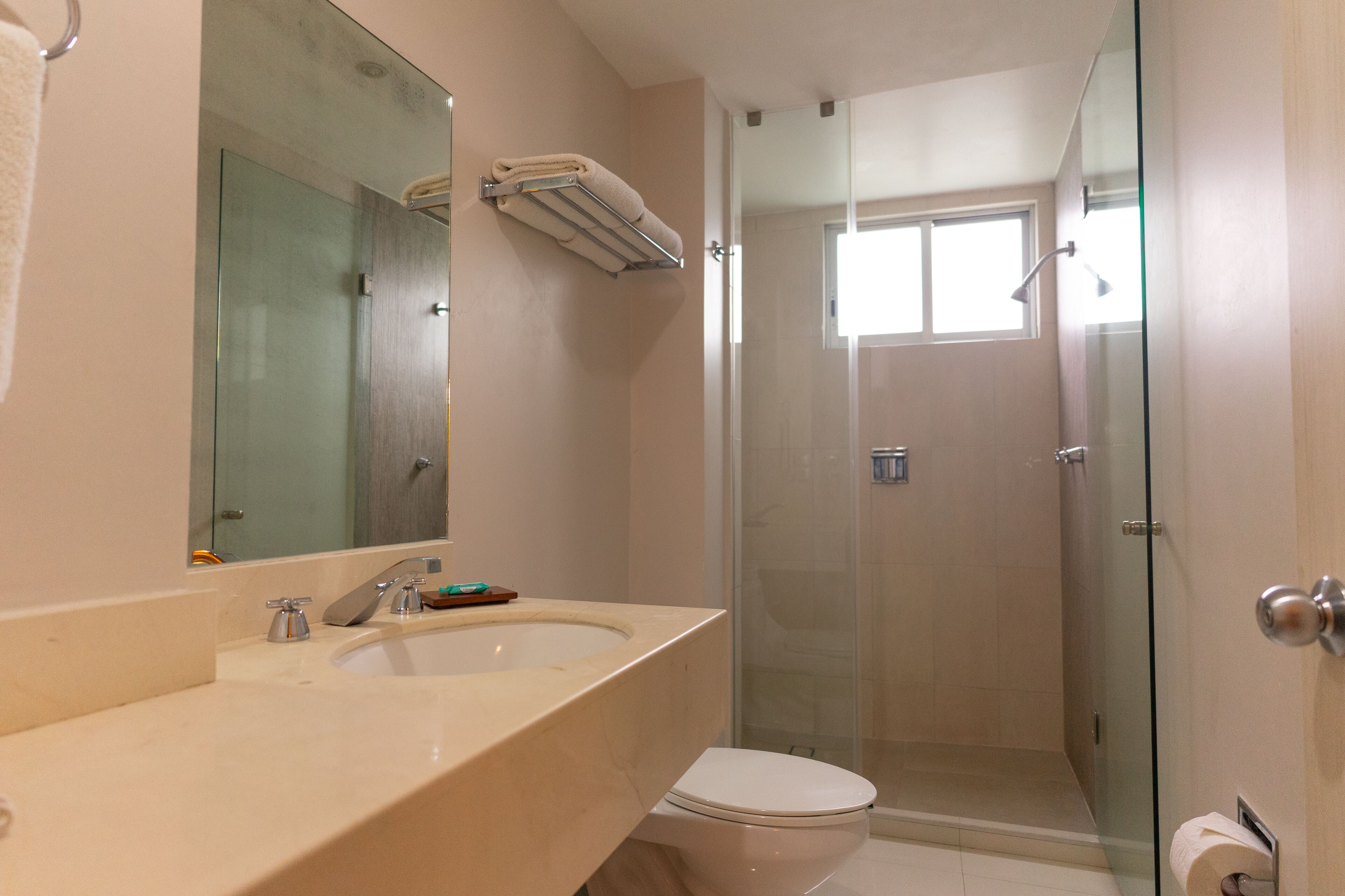 Un baño con cabina de ducha de vidrio, inodoro y lavamanos con espejo.
