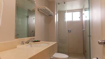 Un baño con cabina de ducha de vidrio, inodoro y lavamanos con espejo.