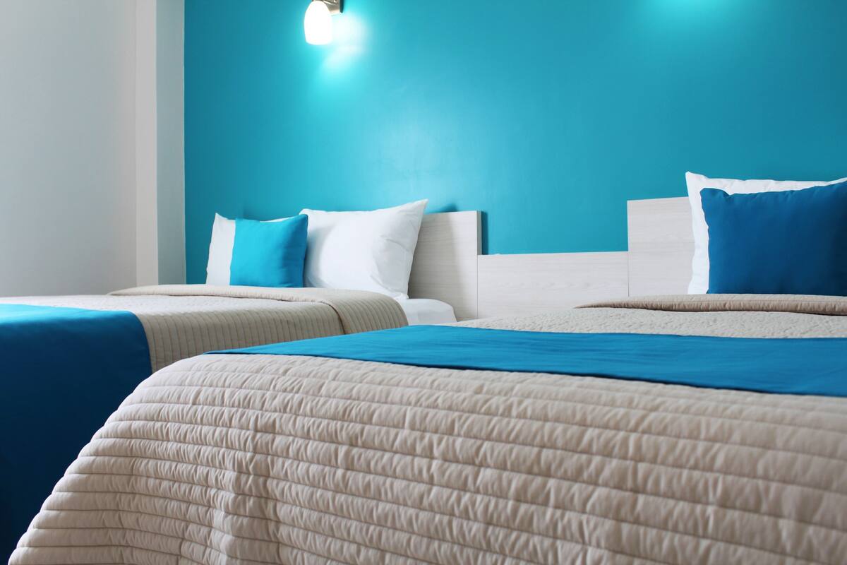 Habitación de hotel con dos camas, una pared de acento color turquesa y una lámpara.