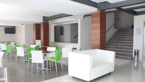 Un espacio interior moderno con un sofá blanco, sillas verdes y un televisor de pantalla plana montado en la pared.