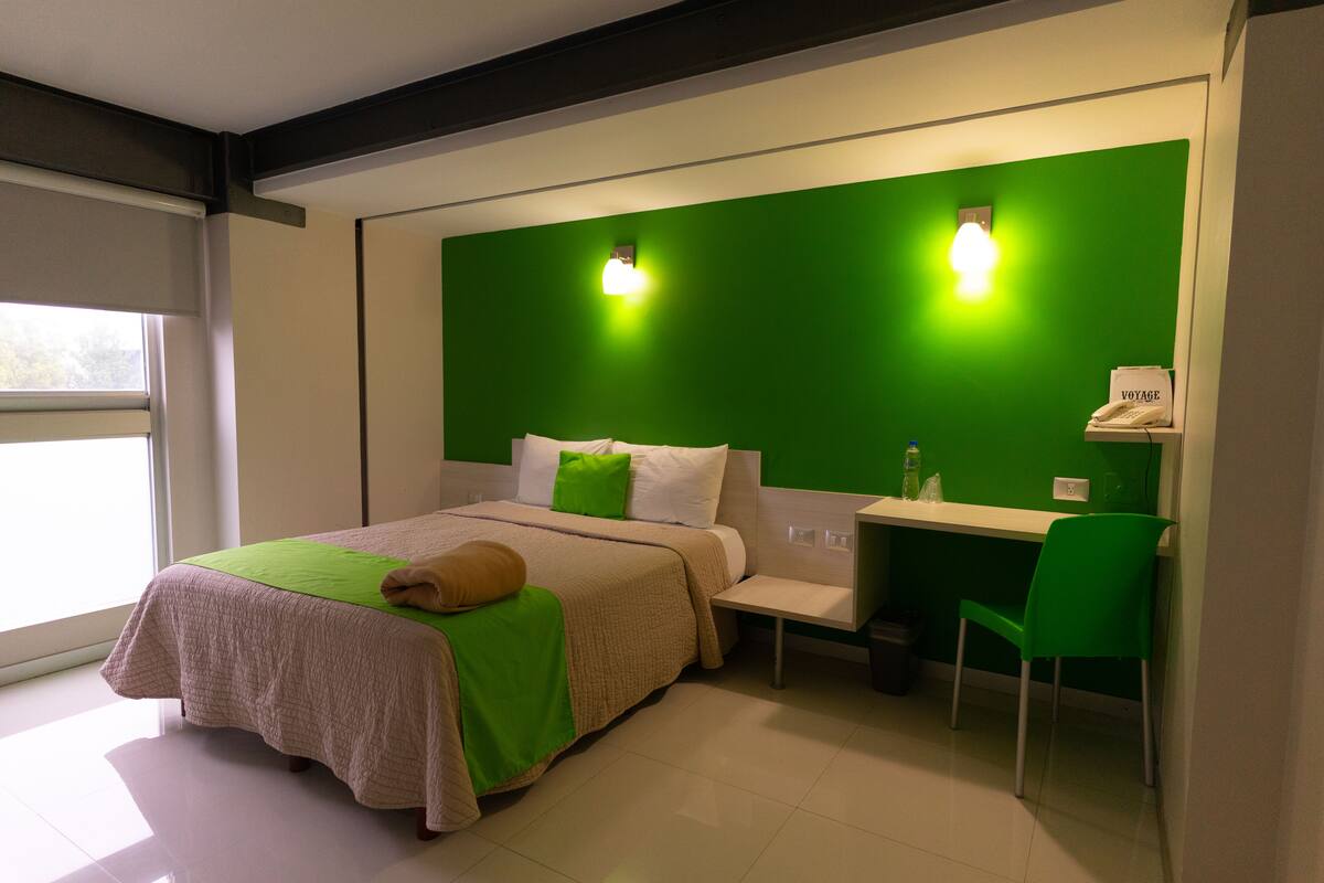 Un dormitorio moderno con una pared de acento verde, una cama con edredón verde y blanco, una mesita de noche, una silla verde y un escritorio con silla.