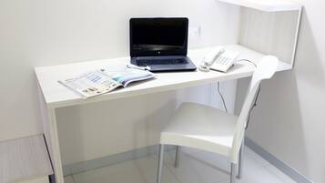 A white desk with a laptop, a telephone, and a magazine.