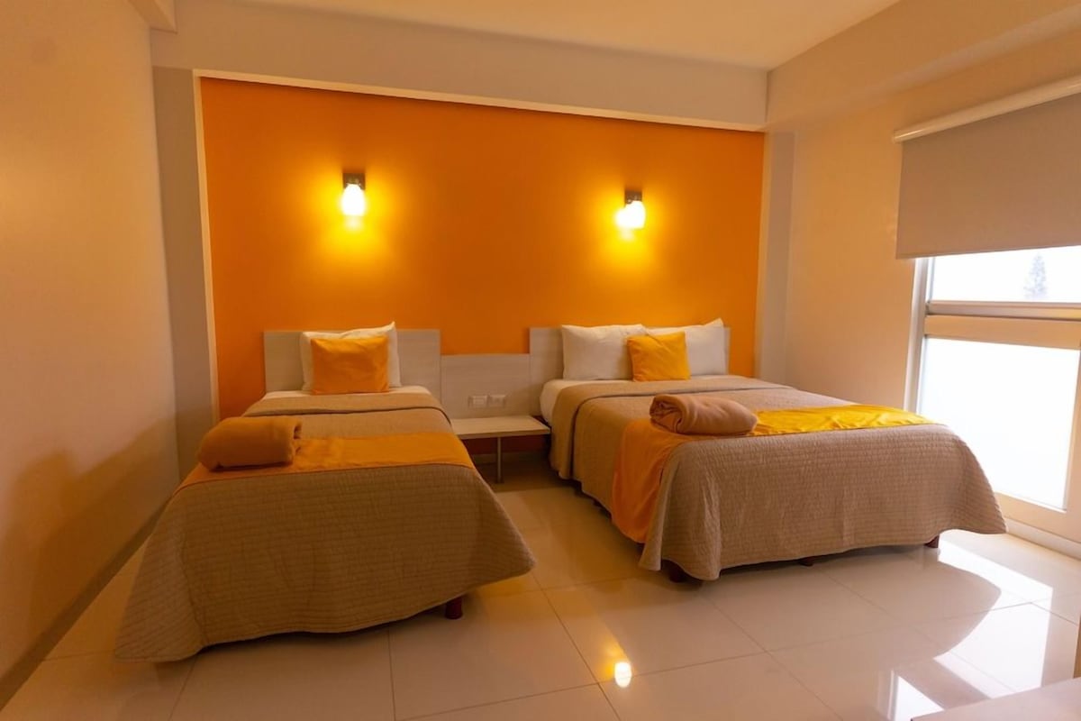 A hotel room with two beds, a nightstand, and a window.