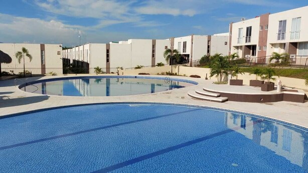 A swimming pool surrounded by modern buildings with a thatched-roof structure nearby. - 5 minutos de Girardot,  casa nuenva amoblada con aire acondicionado (Ricaurte)