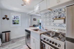 Une cuisine moderne avec des meubles blancs, un lave-vaisselle en acier inoxydable, une cuisinière à gaz et un crédence décorée.