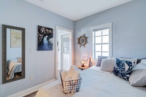 Une chambre à coucher avec un lit, un gouvernail de bateau fixé au mur, une carte encadrée et un panier rempli de serviettes.