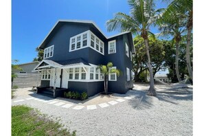Step up to the entrance of this charming two-story house, surrounded by lush palm trees and a serene grassy area.