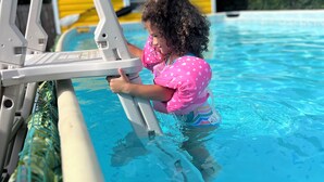 A child in a pool using a pool ladder. - The Sunrise House (Port Richey)