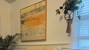 A living room with a beige sofa, a woven basket with a lit candle, and a painting on the wall. - The Sunrise House (Port Richey)