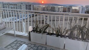 A balcony with a view of a sunset, a white railing, and potted plants.