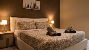 A neatly made bed with patterned bedding, two bedside lamps, and a painting of sailboats on the wall.