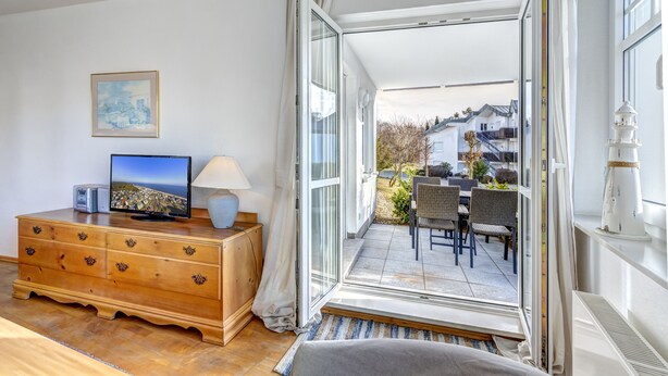 Een kamer met een houten dressoir, een televisie en een raam met toegang tot een terras buiten, inclusief een tafel en stoelen.