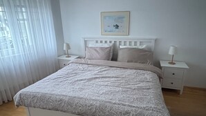 Een slaapkamer met een bed, twee nachtkastjes, een raam met gordijnen en een ingelijste foto aan de muur.