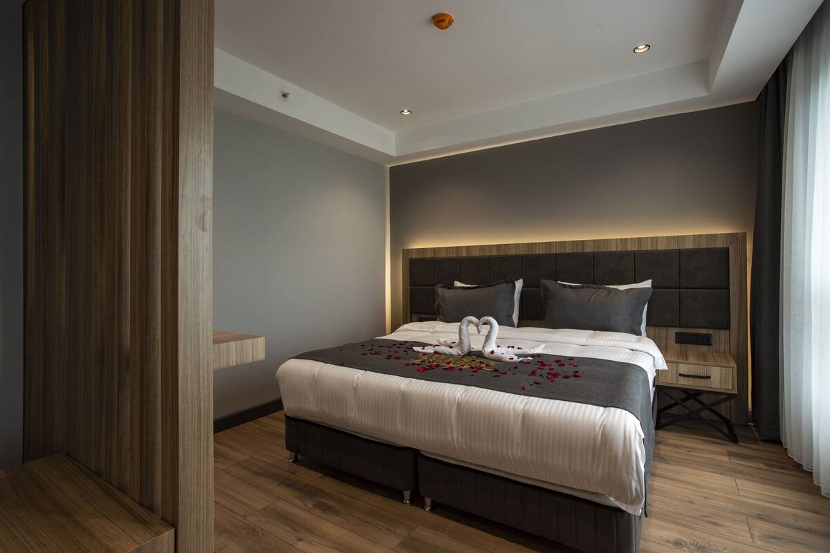 Una habitación de hotel moderna con una cama grande, una mesita de noche de madera y un cabecero con iluminación integrada.