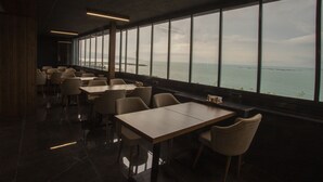 A restaurant with a view of the sea, featuring tables and chairs arranged along the windows. - Gursoy Exclusive Hotel (Arsin)