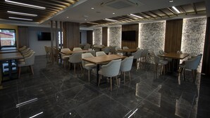 Un espace repas moderne doté de plusieurs tables et chaises, d’un téléviseur à écran plat fixé au mur et d’un mur à la texture de pierre.